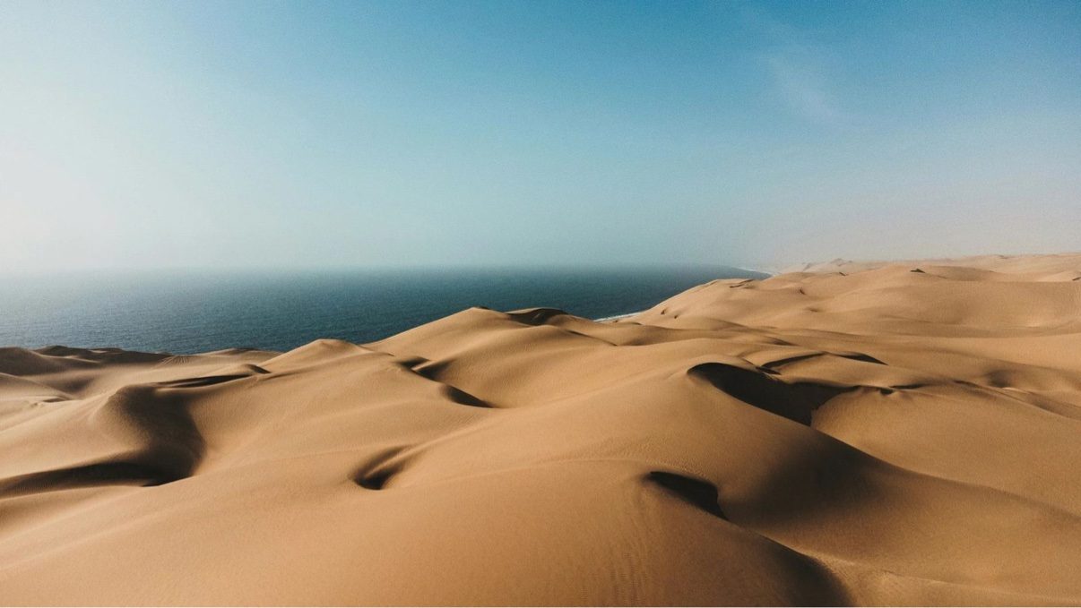 Aerial view of Sandwich Harbour, Namibia, where golden desert dunes meet the Atlantic Ocean